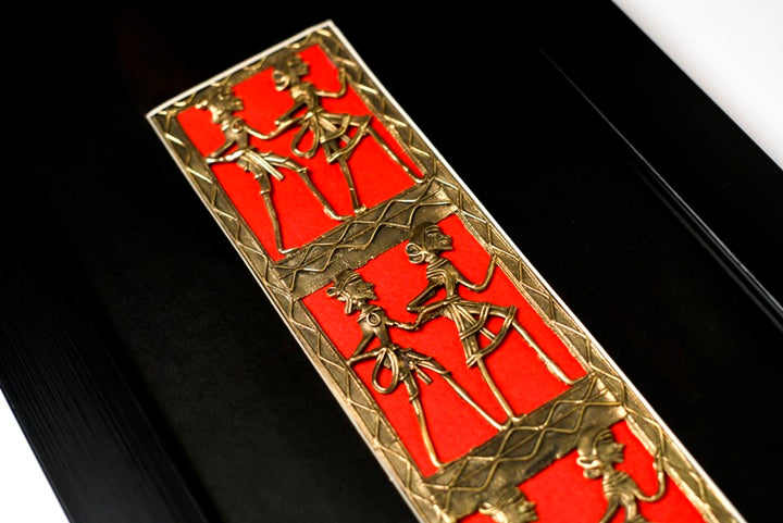 Close-up of intricate Dhokra brass craftsmanship depicting synchronized folk dancers on a deep red backdrop.